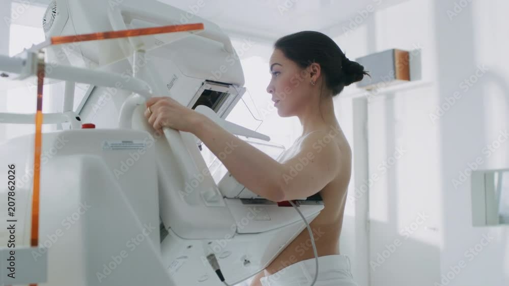 In the Hospital, Back View Shot of Topless Female Patient Undergoing Mammogram Screening Procedure. Healthy Young Female Does Cancer Preventive Mammography Scan. In the Hospital, Back View Shot of Topless Female Patient Undergoing Mammogram Screening Procedure. Healthy Young Female Does Cancer Preventive Mammography Scan.
