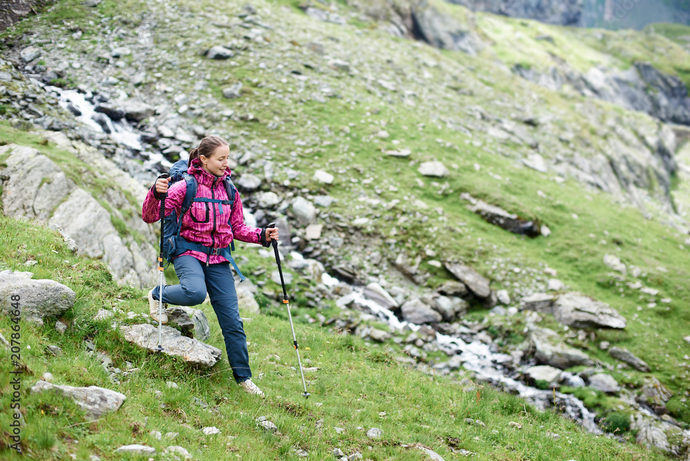 Overcoming obstacles. Young female climber walking down grassy rocky hill in green beautiful mountains in Romania. Woman tourist breathtaking view amazing nature healthy lifestyle