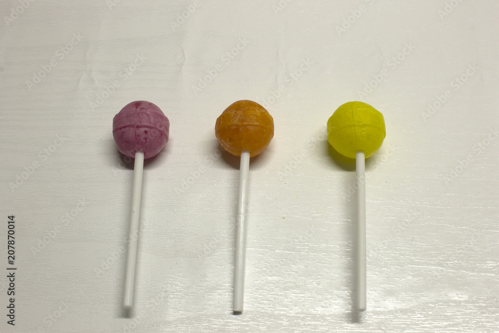 Three purple,yellow and Orange Lollipops isolated on a White textured background Three purple,yellow and Orange Lollipops isolated on a White textured background