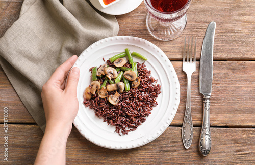 Woman holding plate with delicious brown rice, mushrooms and green beans