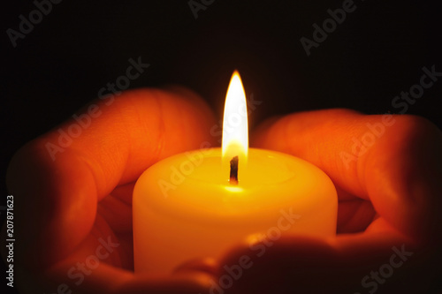 Young person holding burning candle in darkness, closeup