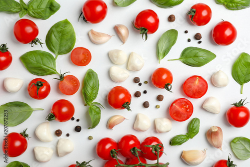 Flat lay composition with tomatoes, mozzarella cheese balls, garlic and basil on light background