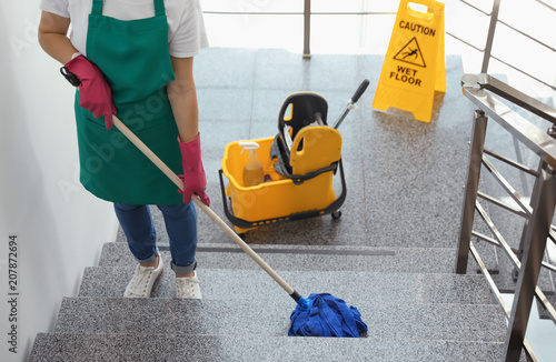 Obraz na plátne Young woman with mop cleaning stairs