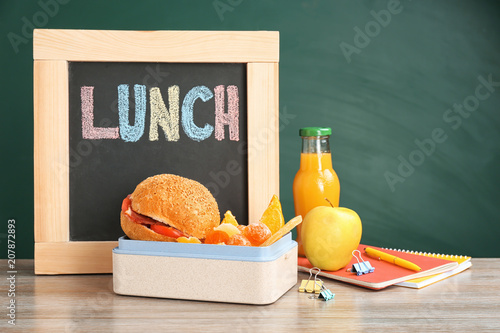 Tableau sur toile Lunch box with appetizing food, small blackboard and notebooks on table