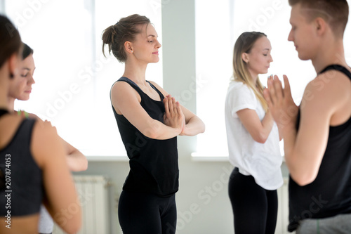 Group of young sporty people practicing yoga lesson, doing meditation exercise, Namaste pose, relaxation after or before working out, indoor close up, yogi students training in sport club © fizkes