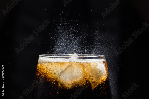A glass of cola beverage with a salt close-up. On a black background.
