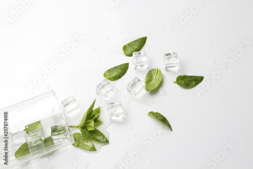 Spilled Glass with refreshing water, mint leaves and ice cubes on a light background