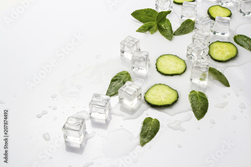 Spilled Glass with refreshing water, cucumber slices, mint leaves and ice cubes on a light background. Flat lay, top view