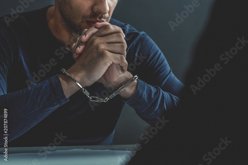 Criminal man with handcuffs in interrogation room photo