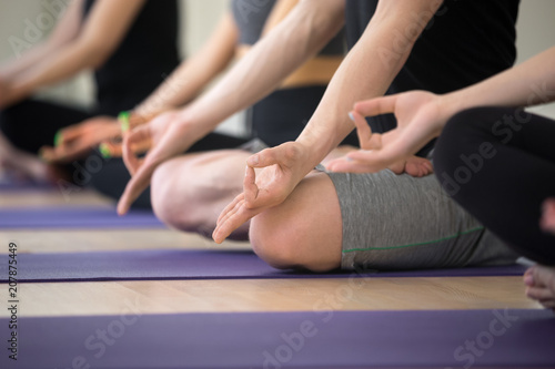 Sporty people practicing yoga lesson, sitting in Sukhasana exercise, Easy Seat pose, working out, indoor close up view, hand with mudra gesture, studio. Mindfulness, wellness, wellbeing concept