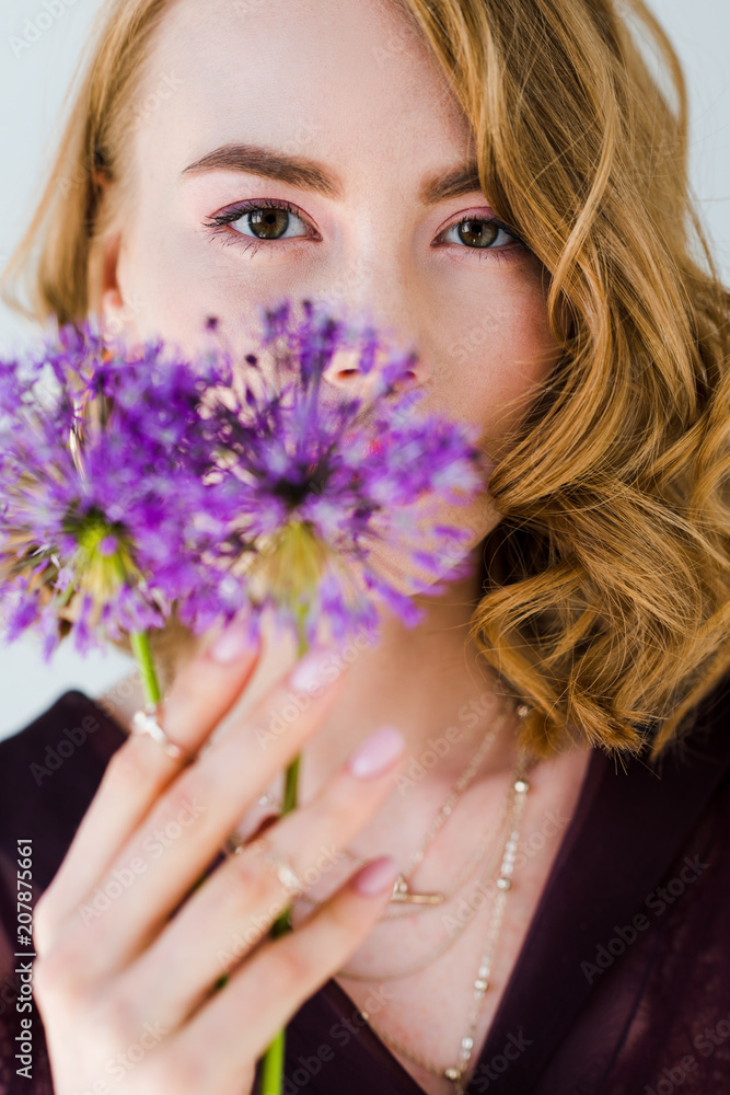 beautiful young woman holding fresh purple flowers and looking at camera isolated on grey beautiful young woman holding fresh purple flowers and looking at camera isolated on grey