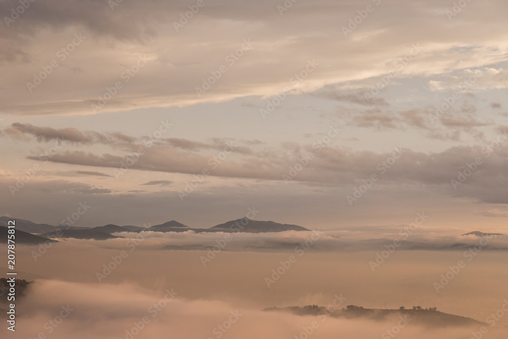 Valley filled by fog at sunset, with beautiful and warm, soft colors and mountains emerging from the fog