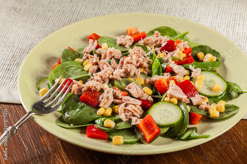 Fresh spinach salad with tuna, cucumber, corn, and red paprika on a plate