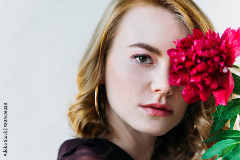 close-up view of girl holding red flower and looking at camera isolated on grey
