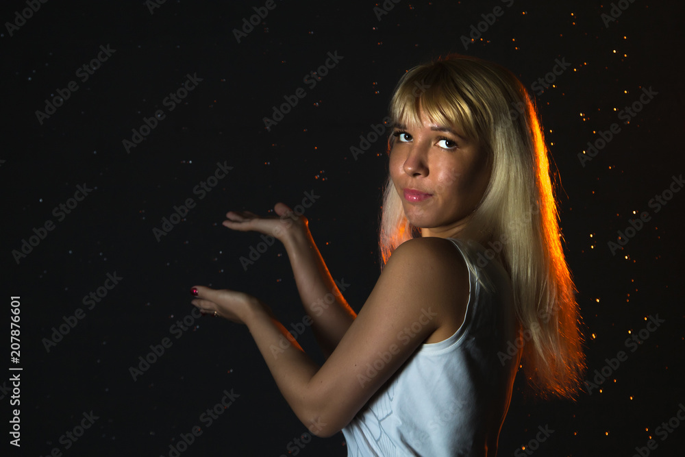Girl in the white shirt and water drops behind and arround her illuminated by light during a photoshoot with water