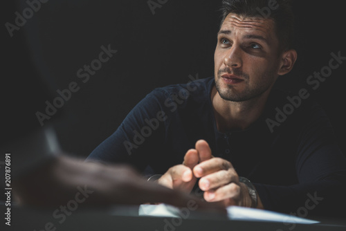 Criminal man with handcuffs in interrogation room