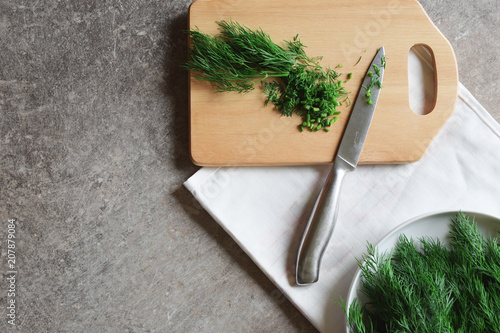 Cut dill and metal knife on chopping board on white towel and grey grunge table background with copy space for text. Cut greens for adding to soup or salad. Preparation of healthy meals concept.