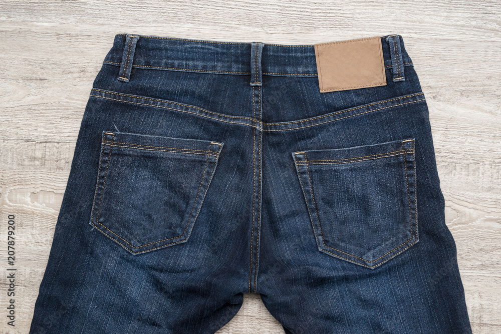 Back of blue jeans on wood background with brown leather label. Back of blue jeans on wood background with brown leather label.