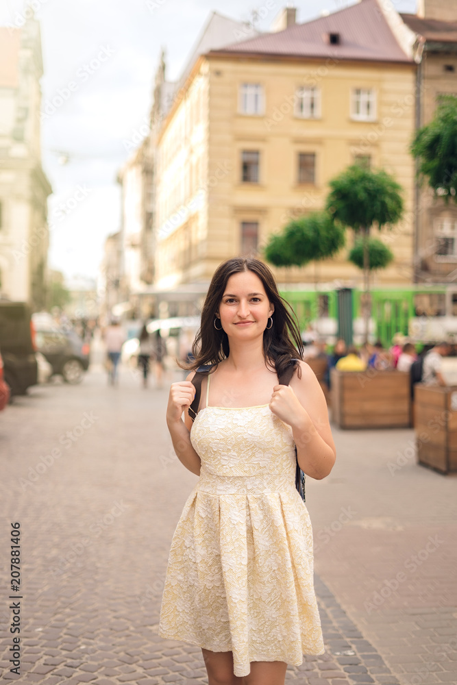 Brunette girl in dress and backpack in city. Girl in yellow summer dress Brunette girl in dress and backpack in city. Girl in yellow summer dress