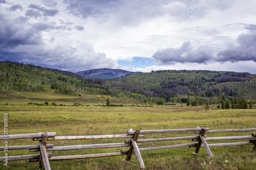 Clouds Hang over the Rocky Mountains with a Wood Fence Built across a Green Meadow in the Foreground in Colorado, USA