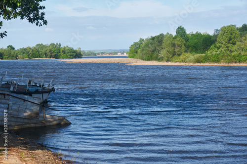 Fototapeta Naklejka Na Ścianę i Meble -  A river on a sunny summer day. On the left is an old boat.