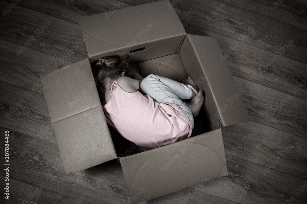 A sad little child lies in a box on the floor. The concept of isolation,  loneliness, running away from problems. Stock Photo | Adobe Stock