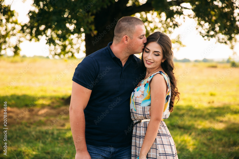 Handsome guy and an attractive girl hug each other near a large green tree. Love story Handsome guy and an attractive girl hug each other near a large green tree. Love story