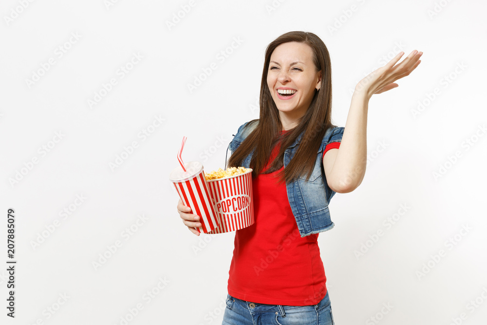 Portrait of young laughing woman in casual clothes watching movie film, holding bucket of popcorn, plastic cup of soda or cola spreading hand isolated on white background. Emotions in cinema concept. Portrait of young laughing woman in casual clothes watching movie film, holding bucket of popcorn, plastic cup of soda or cola spreading hand isolated on white background. Emotions in cinema concept.