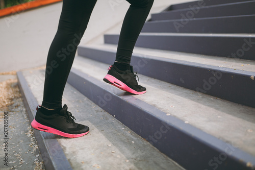 Cropped close up of woman legs in sportswear, black and pink sneakers doing sport exercises, climbing on stairs outdoors. Fitness, healthy lifestyle concept. Copy space for advertisement.