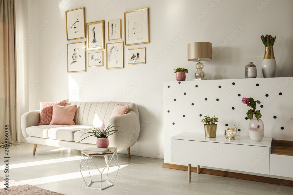 Obraz premium Side angle of a living room interior with white sofa, coffee table, cabinet, art collection and plants