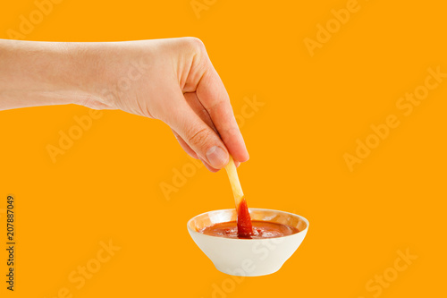 Hand holds fries in socket cup with ketchup isolated on orange background.
