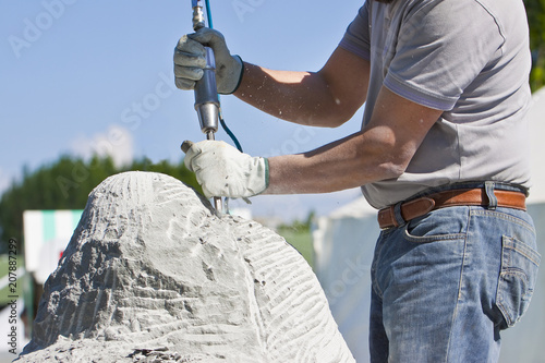 Young man at work with compressed air chisel and protective gloves to carving a stone block