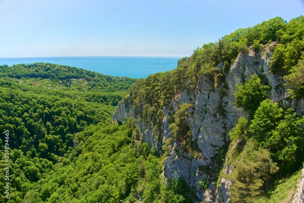 A mountain range not far from the city of Sochi. High rocks and a cliff beneath them. Eagle rocks. Green forest below.