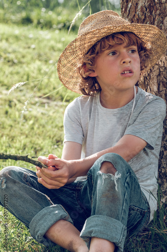 Close up of boy sitting near tree trunk photo