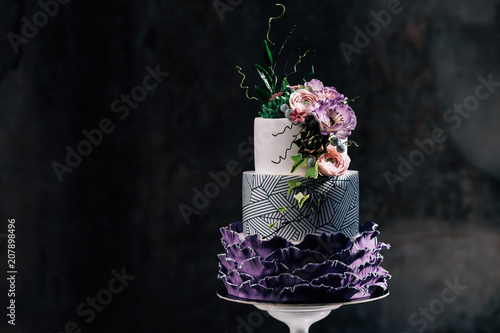 Purple happy birthday cake with beautiful flowers. Dozen of violet cakes with gold and fruits. Exquisite desserts.Tasty white tired cake decorated with violet flowers