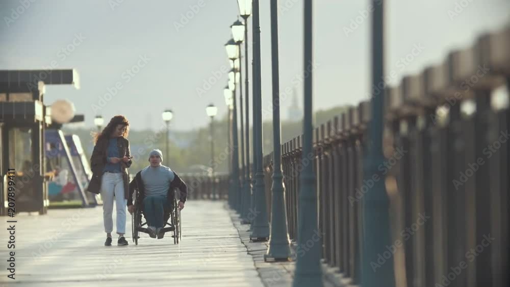 Disabled man in a wheelchair walking together her girlfriend on the quay Disabled man in a wheelchair walking together her girlfriend on the quay