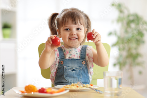 Healthy kids nutrition concept. Cute toddler girl sitting at table with plate of salad, vegetables, pasta in room. Child eating healthy food.