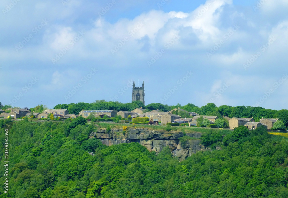 the pennine village of heptonstall viewed from across the calder valley with historic church houses and surrounding woodland and steep rocky hills