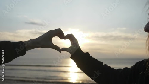 Close up of two lover hands making a heart shape while enjoying sunset and then holding hands romantically in slow motion