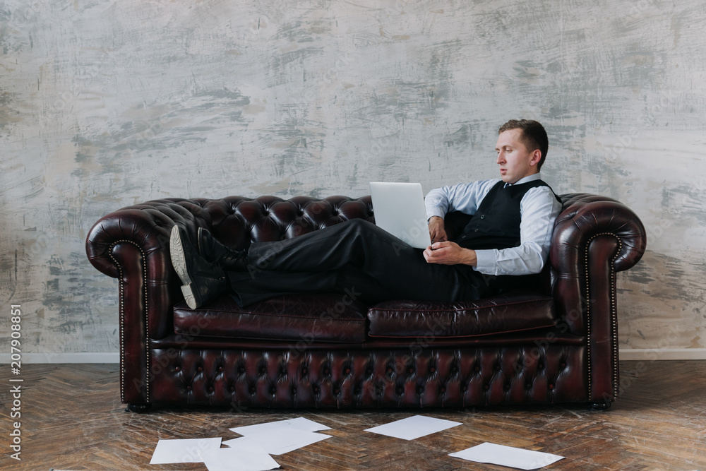 attractive young man in a suit sitting on a retro couch.Rich businessman  sitting quiet on sofa in restaurant.. Handsome luxury man having secret  concerning mafia. Wealth, luxury concepts. Stock Photo | Adobe