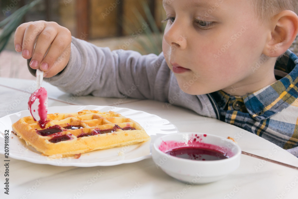 A little boy eats dessert (Belgian waffles with jam) in a cafe. A little boy eats dessert (Belgian waffles with jam) in a cafe.