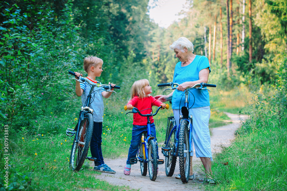 Obraz premium happy grandmother with kids riding bikes in nature