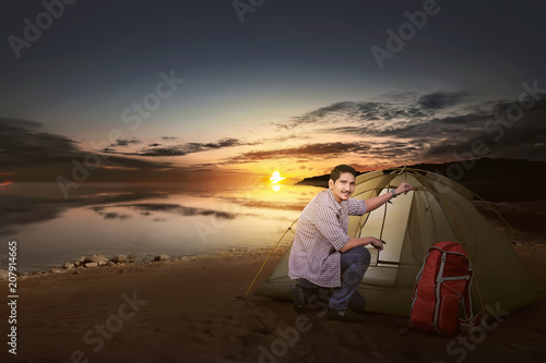 Smiling asian traveler man with backpack set up a tent