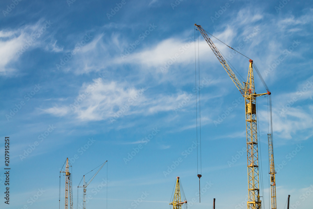 Big tower cranes against the blue sky. Background image of construction equipment close-up with copy space. Build of city. Big tower cranes against the blue sky. Background image of construction equipment close-up with copy space. Build of city.