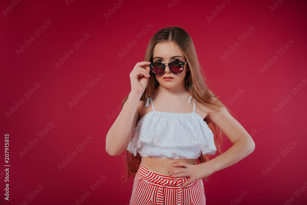 fashion concept - portrait of a beautiful little girl in big hat and sunglasses.Stylish girl in sunglasses, with long hair in shorts and a white top, on a summer vacation fashion concept - portrait of a beautiful little girl in big hat and sunglasses.Stylish girl in sunglasses, with long hair in shorts and a white top, on a summer vacation