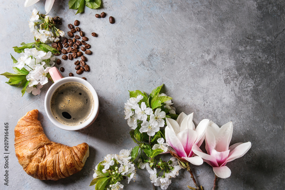 Pink mug of black espresso coffee, french croissant, cream and spring flowers magnolia, blooming cherry branches over grey texture background. Top view, space. Spring greeting card, wallpapers Pink mug of black espresso coffee, french croissant, cream and spring flowers magnolia, blooming cherry branches over grey texture background. Top view, space. Spring greeting card, wallpapers
