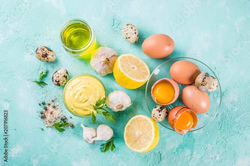 Homemade mayonnaise sauce with ingredients - lemon, eggs, olive oil, spices and herbs, light blue background copy space above