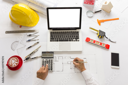  Close-up Architect or engineer hands using calculator and another hand writing to blueprint on laptop, dividers, pencil, ruler and engineering tools on the table. 