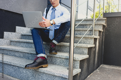 cropped shot of young businessman sitting on stairs and using laptop