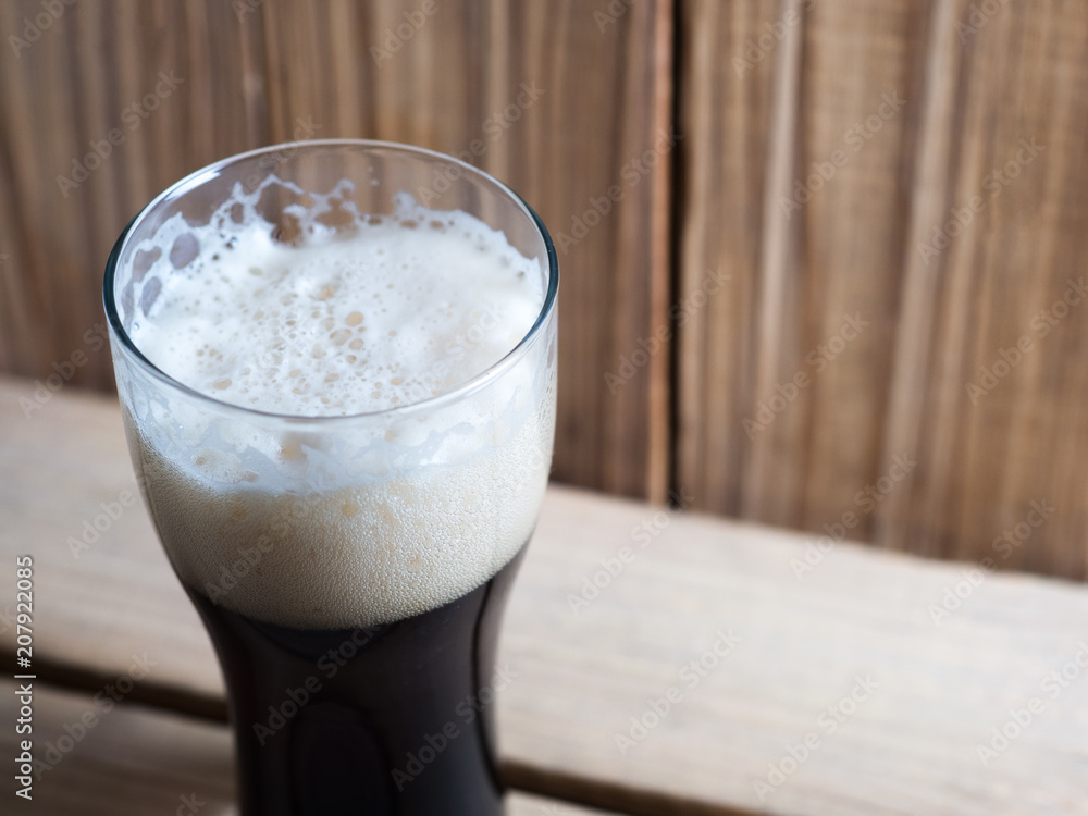 A glass of cold dark beer on a wooden table A glass of cold dark beer on a wooden table